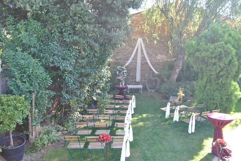 Vista general de la cerimònia al jardí: cadires, arc de teles al fons i taula alta granat