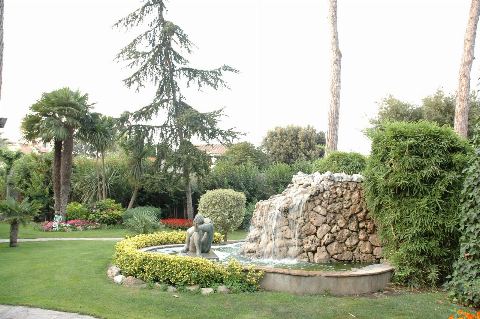 Fuente con cascada de piedra y una escultura, rodeada de césped y palmeras