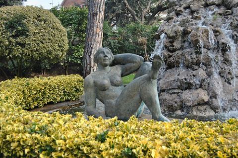 Escultura de una mujer recostada frente a la cascada, entre arbustos amarillos