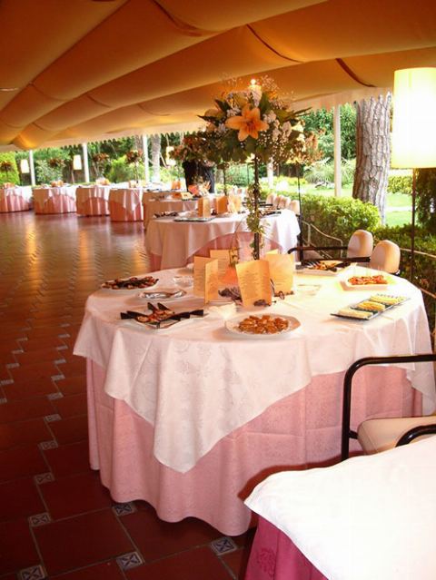 Mesa redonda con mantel rosa y centro floral bajo el toldo