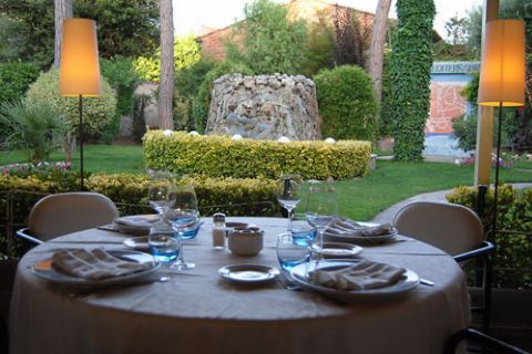 Mesa puesta con lámparas de pie, el jardín y la fuente al fondo
