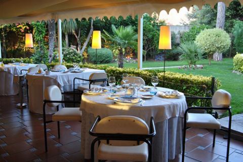 Mesas puestas bajo el toldo con lámparas encendidas y el jardín detrás