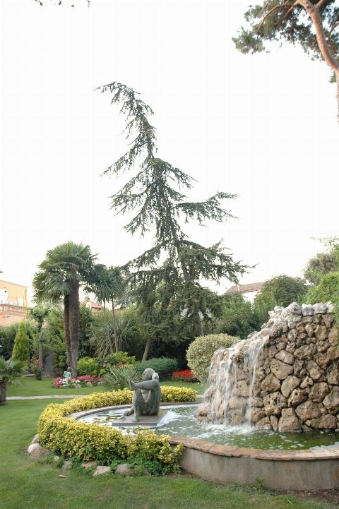Fuente con cascada y escultura rodeada de césped y palmeras, en formato vertical