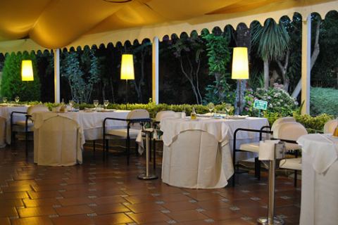 Terraza cubierta de noche con lámparas encendidas y mesas puestas
