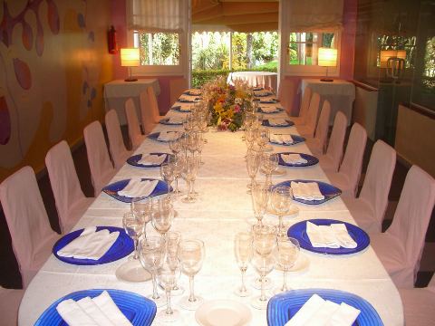 Mesa larga puesta con platos azules, copas y un ramo de flores