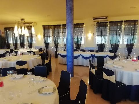 Sala con columna azul, mesa presidencial y mesas redondas al fondo